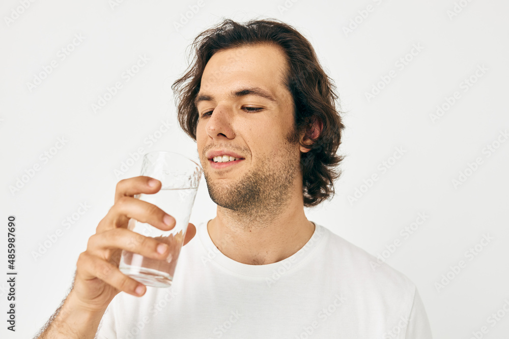 Attractive man in a white T-shirt glass of water isolated background Attractive man in a white T-shirt glass of water isolated background