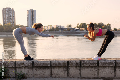 Two woman exercise and stretching outside near the river