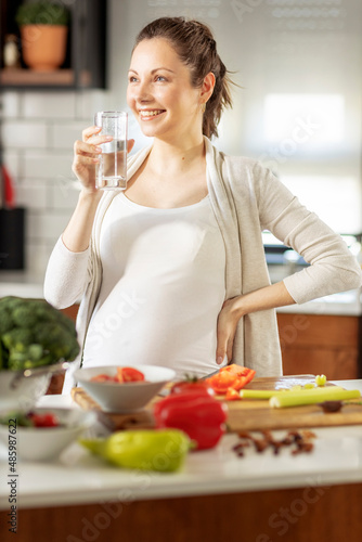Pregnant woman in the kitchen with glass of water on hand prepare healthy food