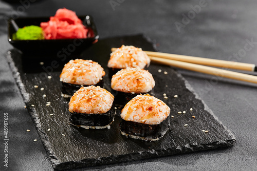 Baked Maki sushi on dark slate. Hot unagi maki with tobiko. Sushi roll with baked cheese, masago and unagi sauce topped. Style concept japanese menu with black background, leaves and hard shadow.