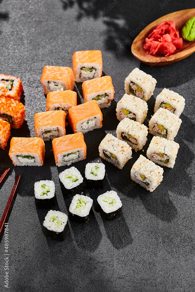 Maki sushi set on dark slate. Maki set with variety rolls. Composition from sushi rolls - philadelphia, california, hosomaki . Style concept sushi menu with black background, leaves and hard shadow.
