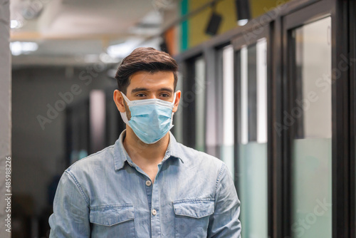 Young businessman wear protection face mask against coronavirus standing in office