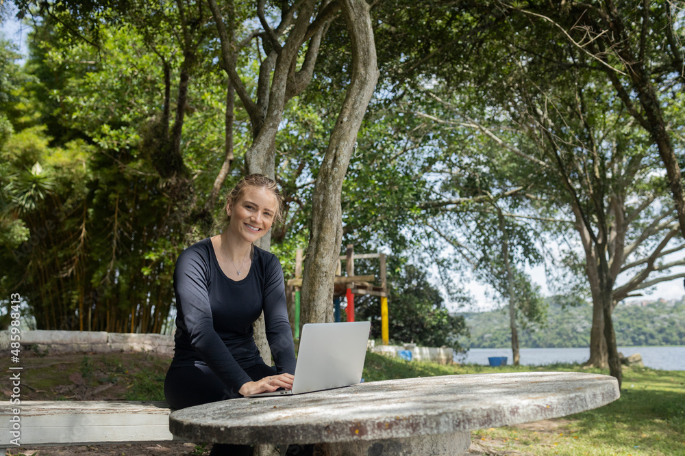 Young woman using a laptop at day time with a green park in the background. High quality photo Young woman using a laptop at day time with a green park in the background. High quality photo
