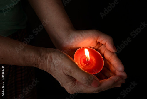 hands around a burning candle in the dark, close-up.