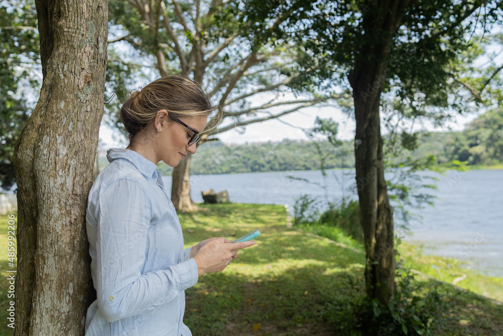Young woman using a smartphone at day time with a green park in the background. High quality photo Young woman using a smartphone at day time with a green park in the background. High quality photo
