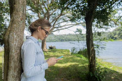 Young woman using a smartphone at day time with a green park in the background. High quality photo