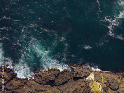 Shooting from a drone. Panoramic shot. Seascape. Turquoise ocean water and white foamy waves crash against the rocky shore. Ecology, geology, geography, climate, environmental protection.