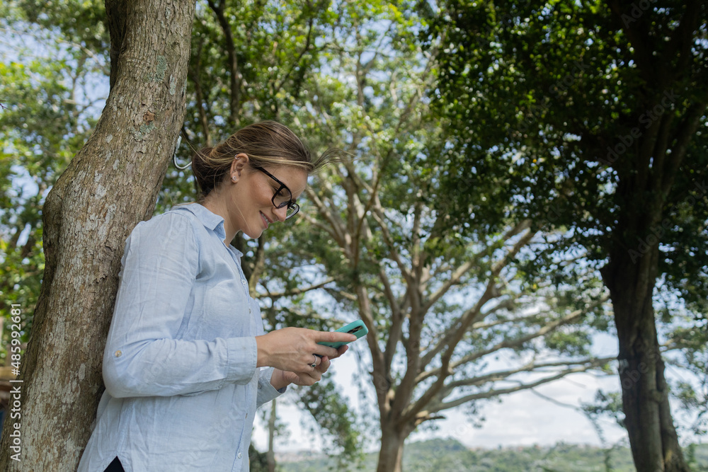 Young woman using a smartphone at day time with a green park in the background. High quality photo Young woman using a smartphone at day time with a green park in the background. High quality photo
