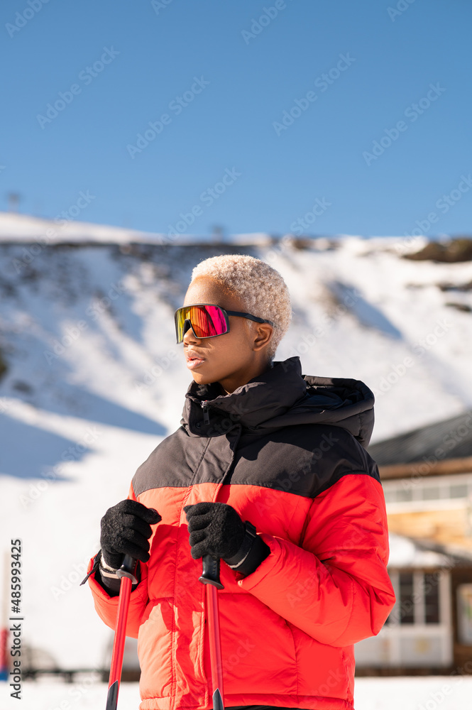 A African American woman with ski poles standing on snowy mountain during winter

