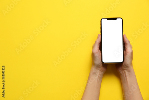 Woman with smartphone on yellow background, top view. Space for text