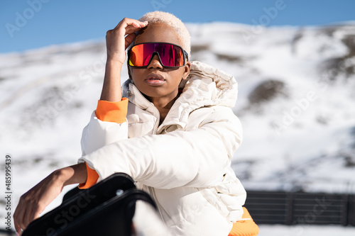 A African American woman wearing goggles standing in snowy mountain during winter
