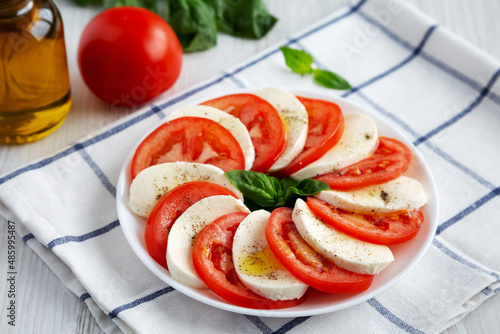 Homemade Caprese Salad with Mozzarella, Tomato and Basil on a white plate, side view.