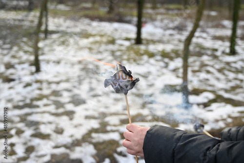 A woman's hand holds a burning paper flower in front of a winter