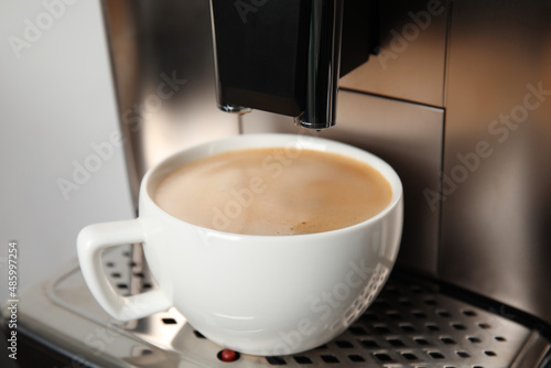 Espresso machine with cup of fresh coffee on drip tray against light background  closeup