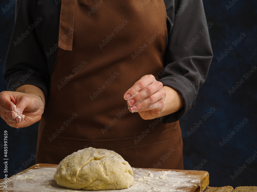 Obraz premium Dough prepared by the chef on a wooden cutting board. Dark background. Minimalism. cooking pasta, pizza. Close-up. Recipes, cooking. Restaurant, home cooking, hotel, pizzeria, bakery.