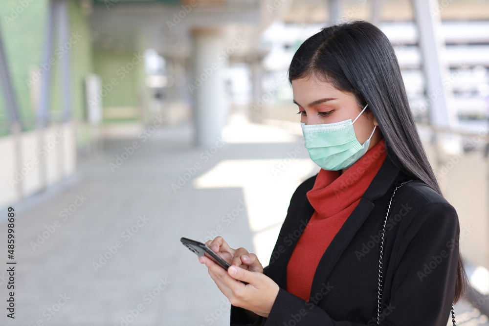 Young asian business woman in business suit with protect mask for healthcare walking on public outdoor and using smartphone. New normal and social distancing concept Young asian business woman in business suit with protect mask for healthcare walking on public outdoor and using smartphone. New normal and social distancing concept