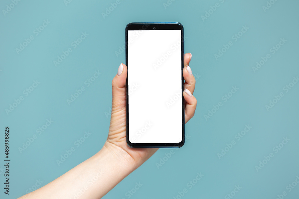 Close-up of a woman's hand with a smartphone on which there is a white screen for advertising, on a blue background. Copy paste. Close-up of a woman's hand with a smartphone on which there is a white screen for advertising, on a blue background. Copy paste.
