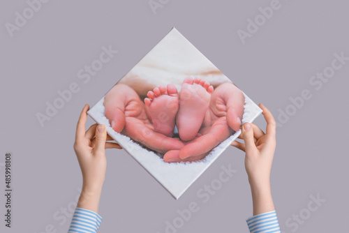 Women's hands hang a family photo of a newborn's legs printed on canvas on a gray wall