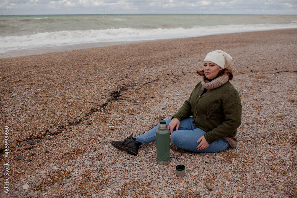 Beatuful woman with over weight body walking in the beach, and drink tea. The plus size model wearing jeans, the warm knitted blanket and sweater. the wind in the bich have fun with hairs Beatuful woman with over weight body walking in the beach, and drink tea. The plus size model wearing jeans, the warm knitted blanket and sweater. the wind in the bich have fun with hairs