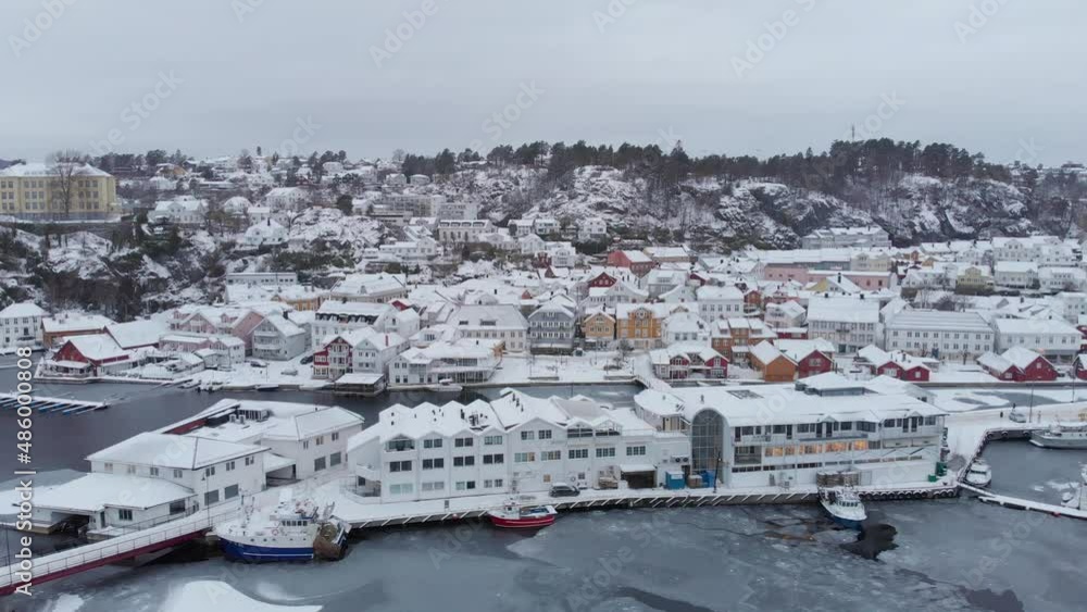 Snow-covered Buildings, Vessels, And Harbor On Frozen Water IIn Kragero Archipelago On A Cloudy Winter Day In Norway. aerial drone sideways Snow-covered Buildings, Vessels, And Harbor On Frozen Water IIn Kragero Archipelago On A Cloudy Winter Day In Norway. aerial drone sideways