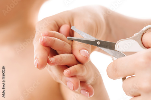 Mother holding little child s hand and cutting nails.