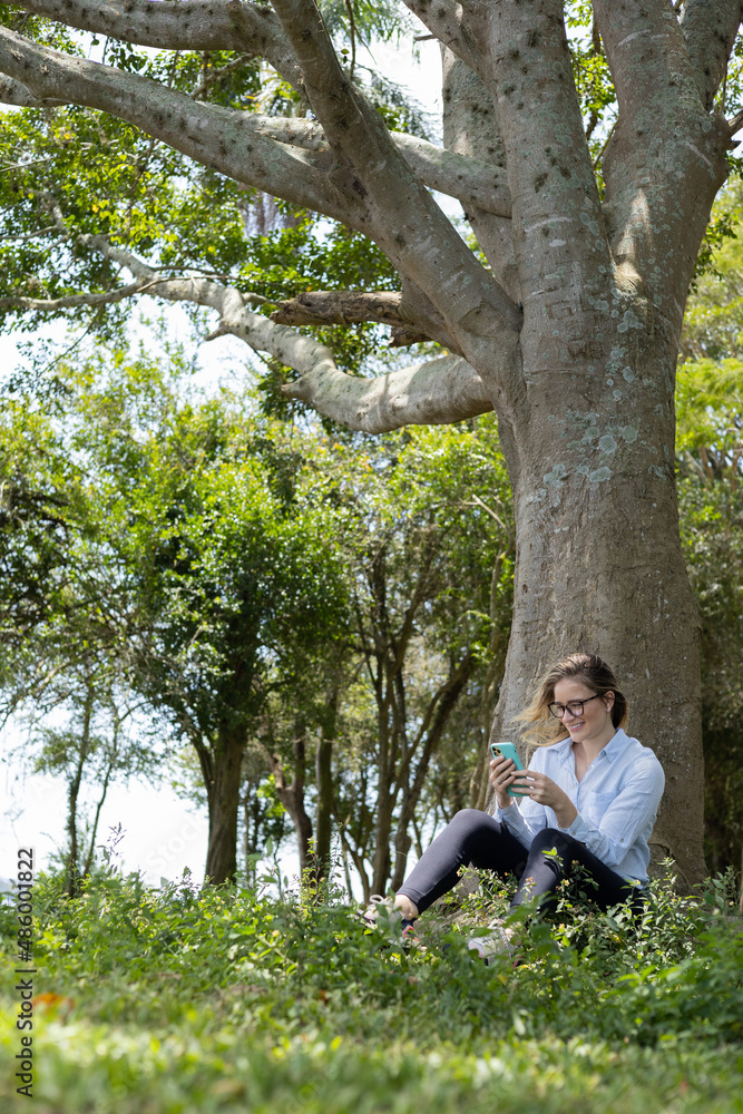 Young woman using a smartphone at day time with a green park in the background. High quality photo Young woman using a smartphone at day time with a green park in the background. High quality photo