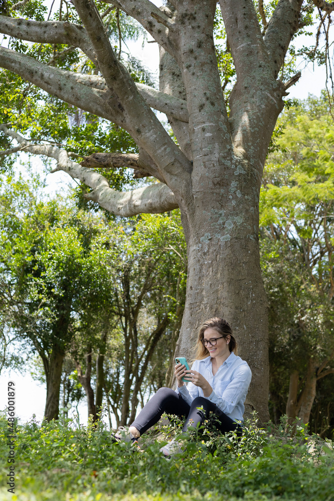 Young woman using a smartphone at day time with a green park in the background. High quality photo Young woman using a smartphone at day time with a green park in the background. High quality photo
