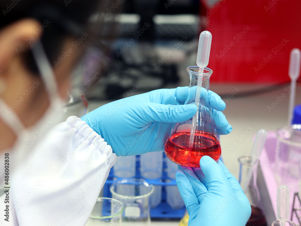 The scientist wears nitrile blue gloves and holds Erlenmeyer flask