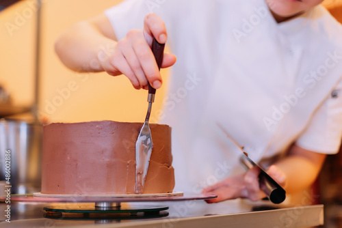 The pastry chef spreads chocolate cream on the cake. The cake consists of three layers of chocolate: white, milky and dark 