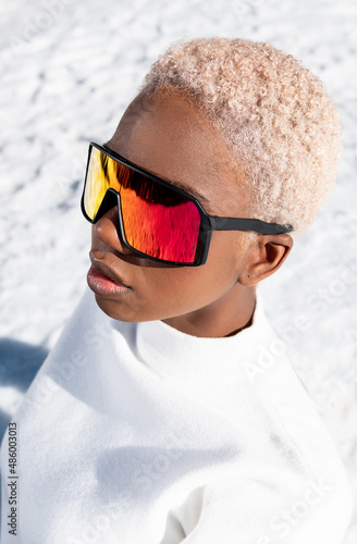 A African American woman with sunglasses sitting on snowy ground during winter