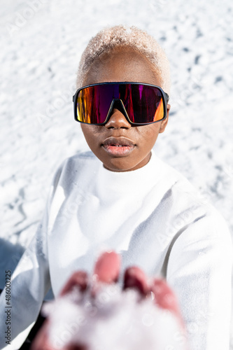 A African American woman with sunglasses sitting on snowy ground during winter