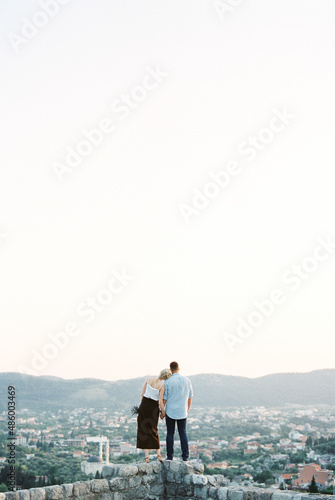 Woman put her head on the man shoulder on a stone wall overlooking the mountains. Back view