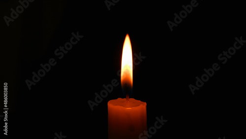 Candle flame on black background. Single lit candle with quite flame. Dramatic burning candle flame on a black background with copy space