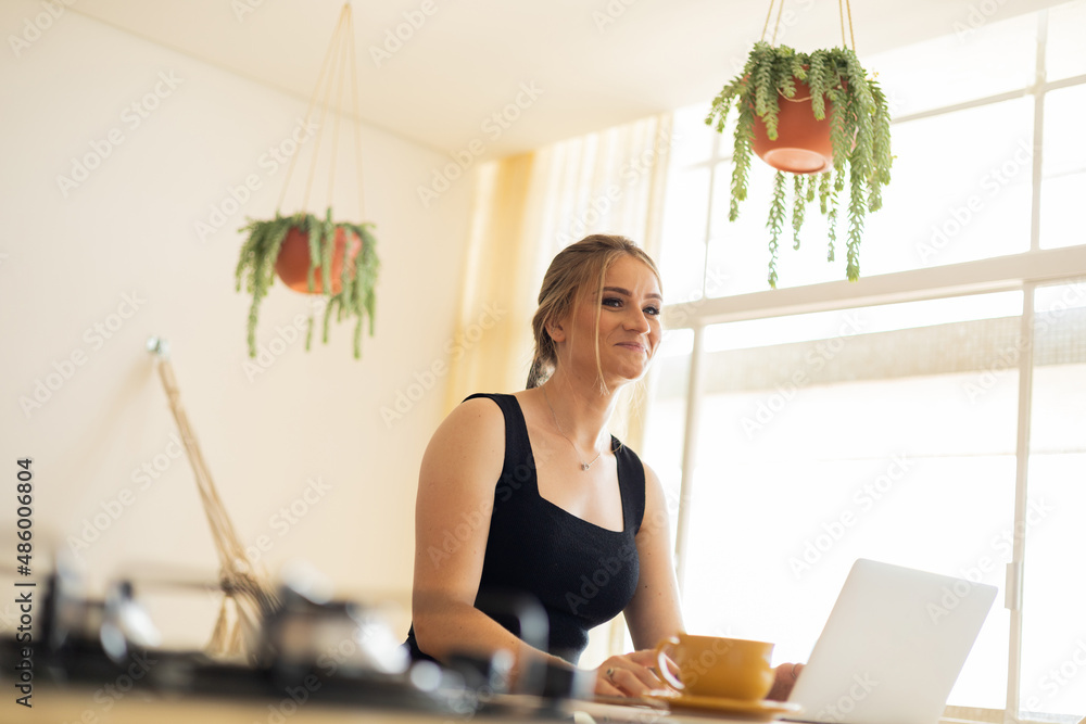 Young woman working at home in her kitchen with laptop and papers on kitchen wooden desk. Home office concept. Young woman working at home in her kitchen with laptop and papers on kitchen wooden desk. Home office concept.