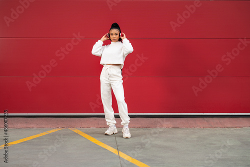 Cheerful African American girl with long black hair dressed in sportswear listening to music