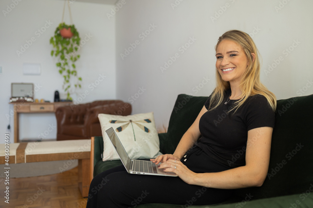 Young woman working at home from her living room couch with laptop on her lap. Home office concept.