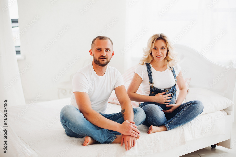 Stylish couple sitting on bad and embracing stomach. Stylish couple sitting on bad and embracing stomach.