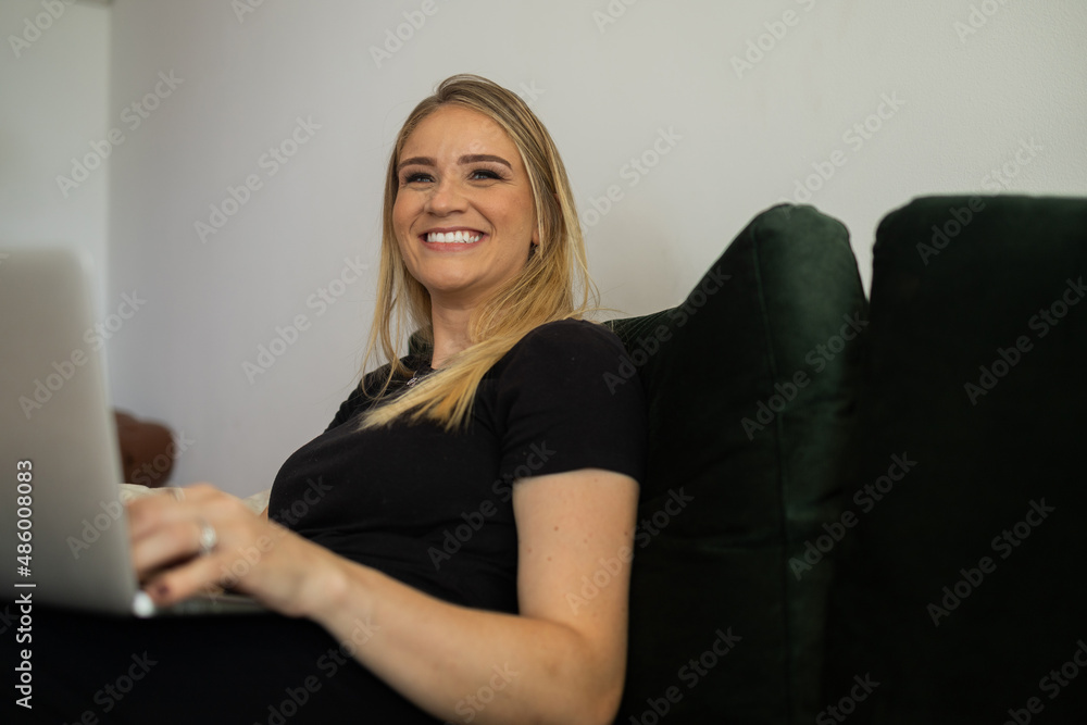 Young woman working at home from her living room couch with laptop on her lap. Home office concept. Young woman working at home from her living room couch with laptop on her lap. Home office concept.