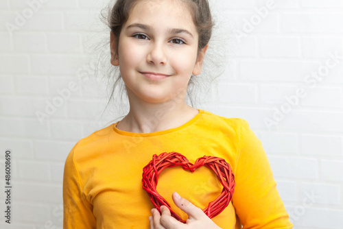 Happy latin young girl holds shape of a heart for mathers or valentines day on a light background with copy space photo