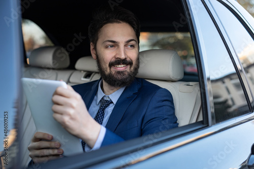 A handsome young businessman in a suit outdoors using his mobile phone is driving in the car