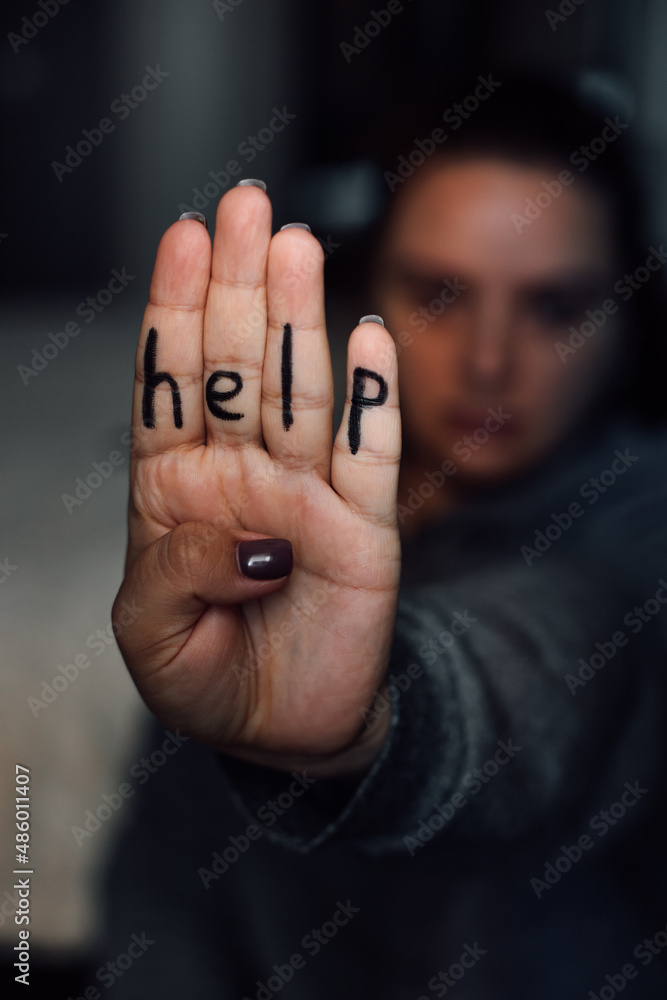 Close-up of hand with letters of word help on each finger with blurry woman  face and body in background. Sign of domestic violence. Physical, mental,  psychological abuse. Victim of beating. Stock-Foto