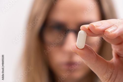 Close up of female hand holding white pill or capsule vitamin supplement close up