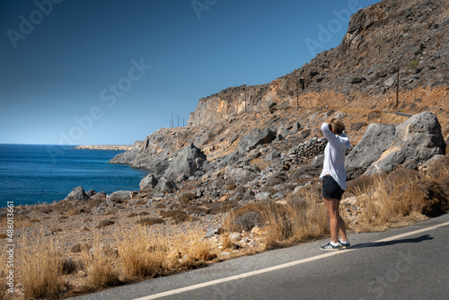 Woman standing on asphalt road looking at sea