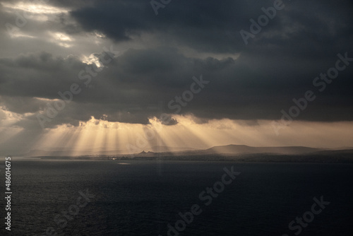 Light rays streaming through dramatic clouds over landscape with sea