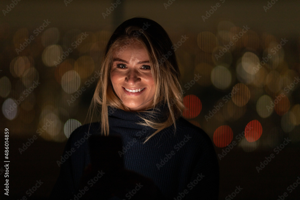 Young woman using a smartphone at night time with city view landscape in the background. High quality photo Young woman using a smartphone at night time with city view landscape in the background. High quality photo