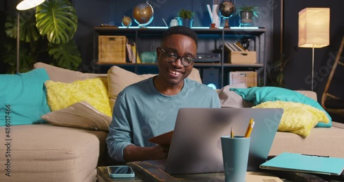 STUDYING ONLINE Happy young smart African male student using laptop web conference talking to teacher at cozy home room. photo