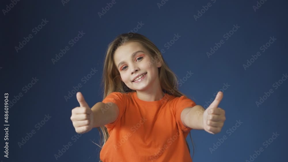 A young teenage girl shows a thumbs up gesture against a blue background. A young teenage girl shows a thumbs up gesture against a blue background.