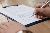 Woman signing contract at wooden table, closeup.