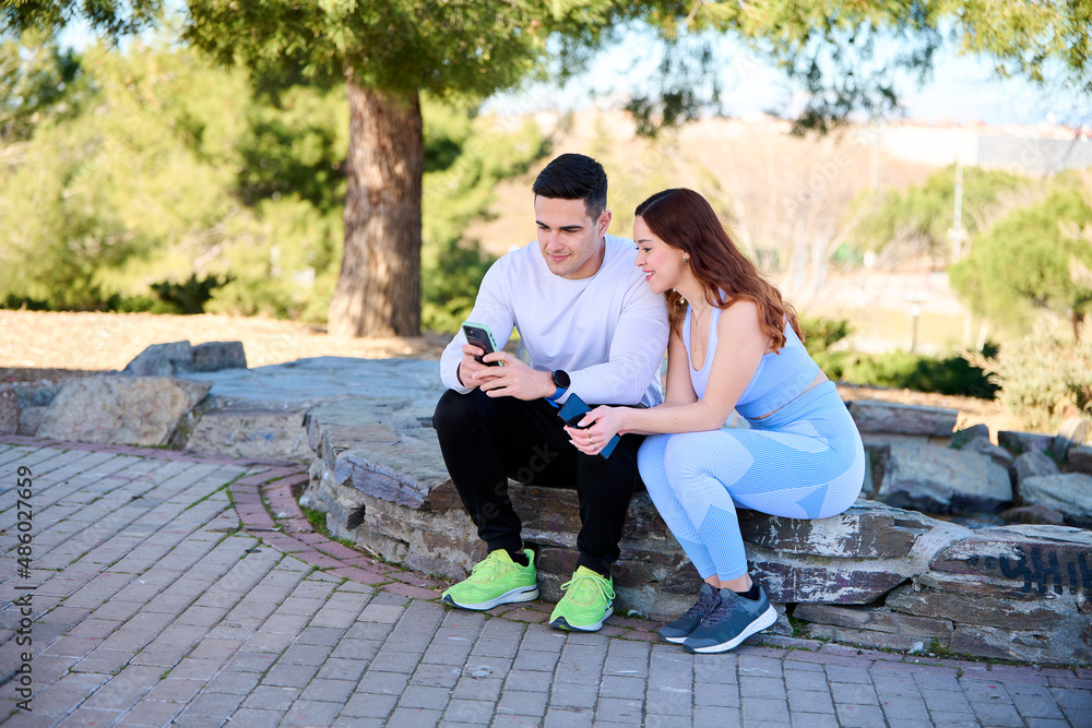 Fototapeta premium Young couple watching online content on a smartphone sitting in a park