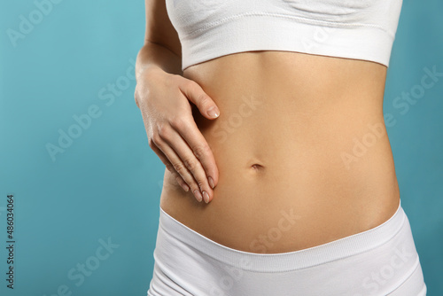 Woman holding hand on belly against light blue background, closeup